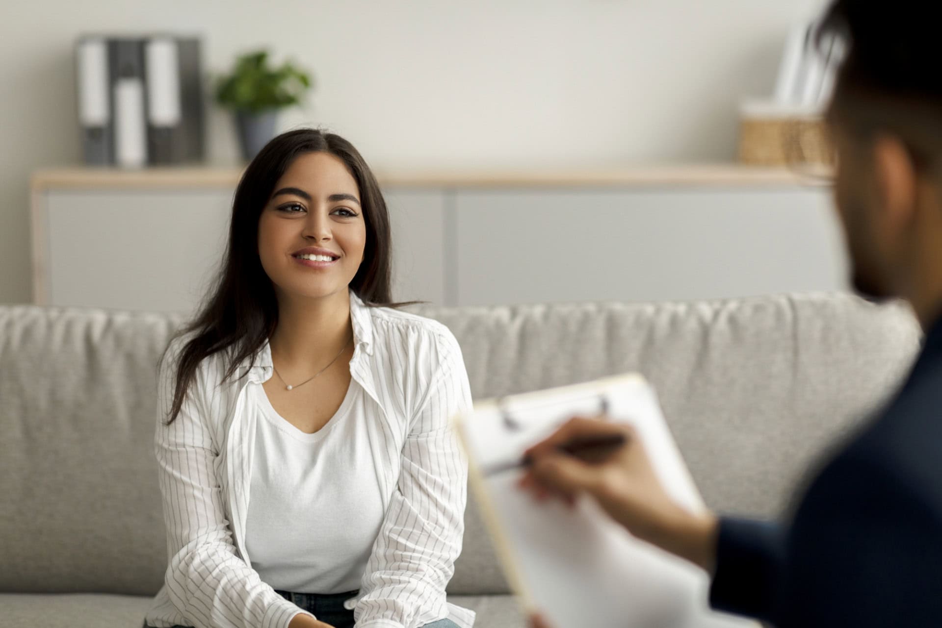 Successful psychotherapy. Happy female client having session with psychologist, smiling, sitting on couch at clinic.